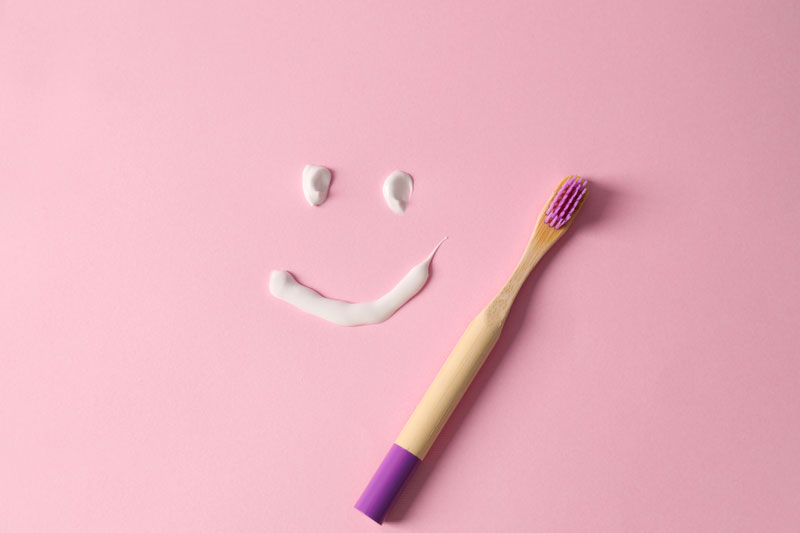 funny-face-made-with-toothpaste-and-brush-on-pink-background-flat-lay